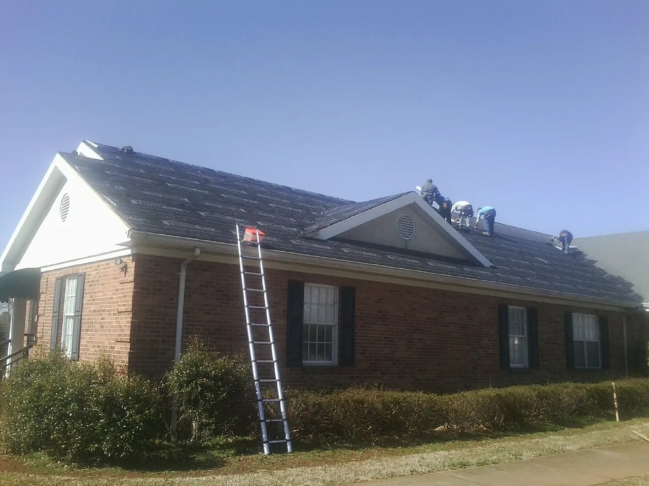 Crew tearing shingles off a brick ranch roof with a ladder set — Emergency Roof Repair work by our crew in Atkinson